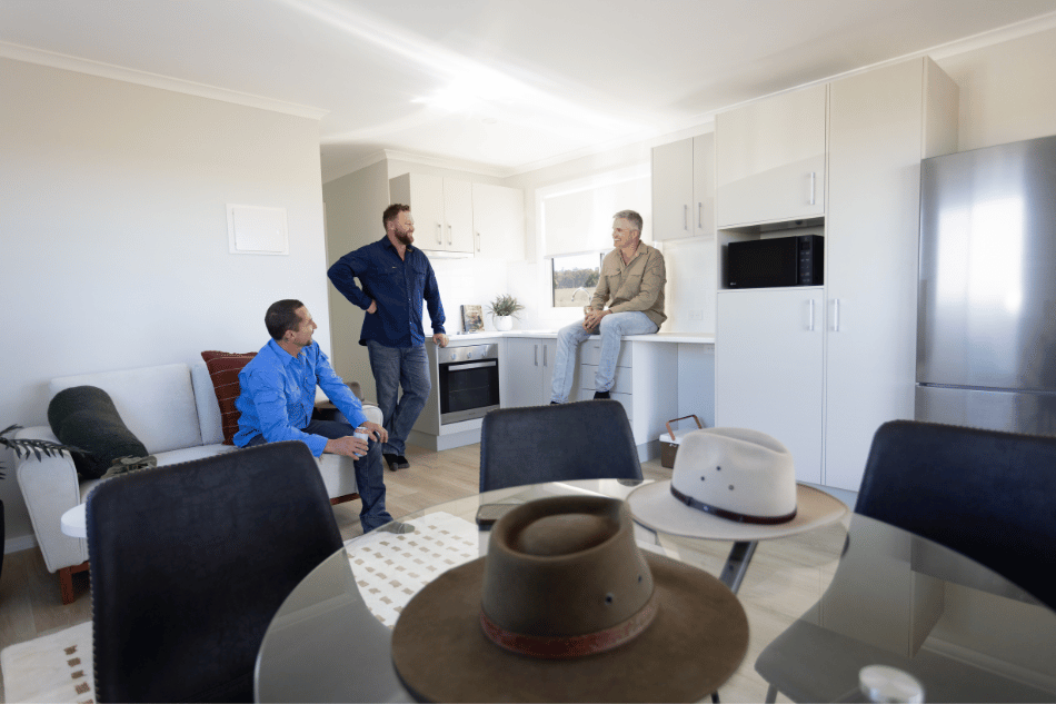 Worker accommodation interior with three men discussing the shared living and kitchen area inside a modern modular unit.