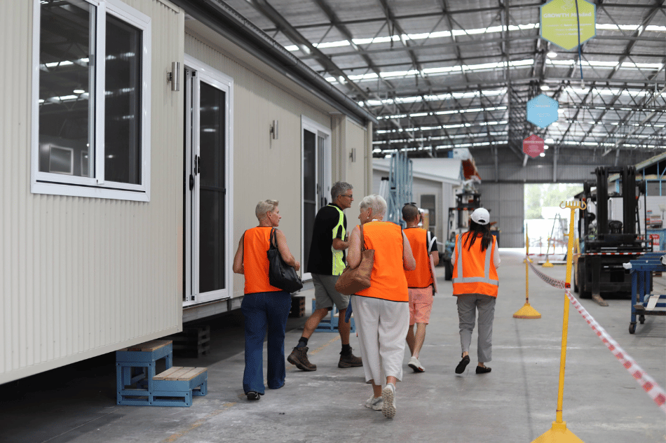 Worker accommodation factory tour showing visitors in safety vests walking beside a modular unit under construction.